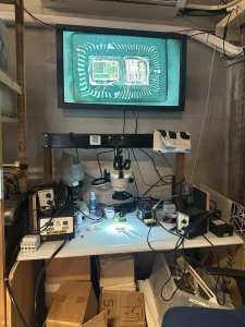 Een werkstation met een microscoop om elektronica te inspecteren. Erboven hangt een beeldscherm met daarop het beeld van wat er door de microscoop te zien is.